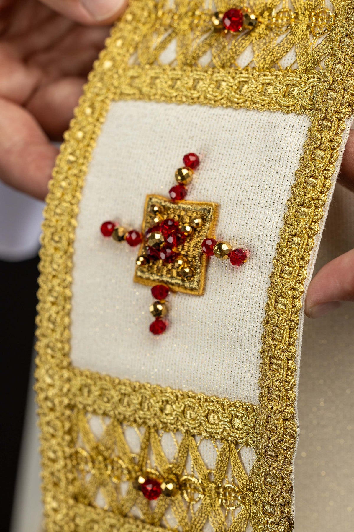 Casula artesanal em detalhe da faixa frontal, com cruz de pedras vermelhas e bordado dourado