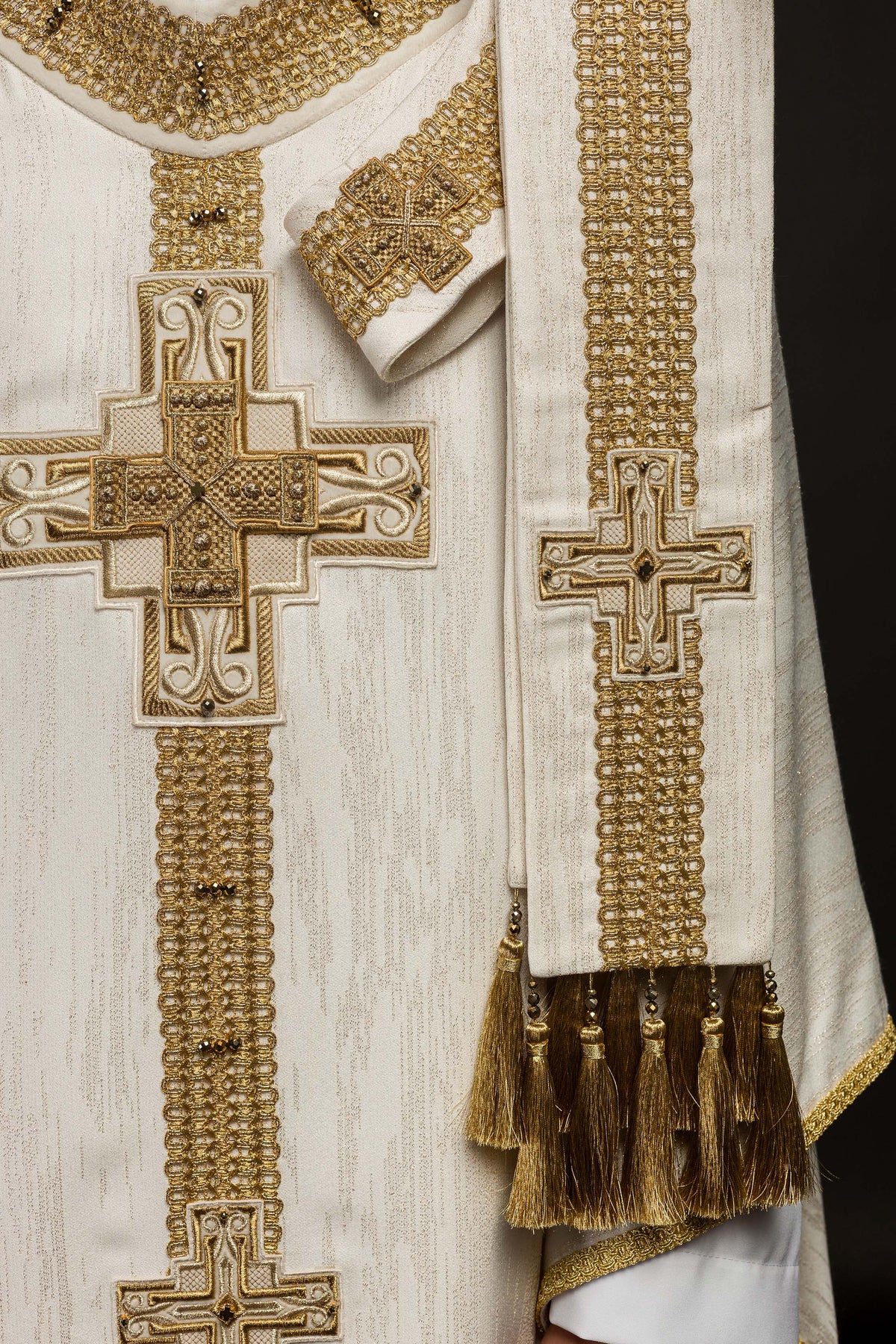 Casula creme com estola frontal visível, cruzes douradas e franjas decorativas