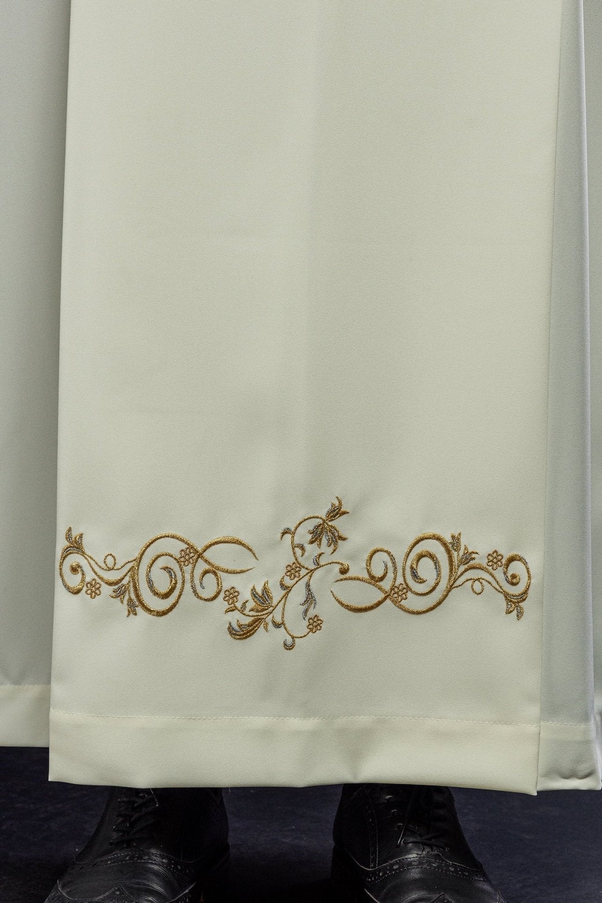 Alva sacerdotal creme em close-up, com bordado floral dourado na barra