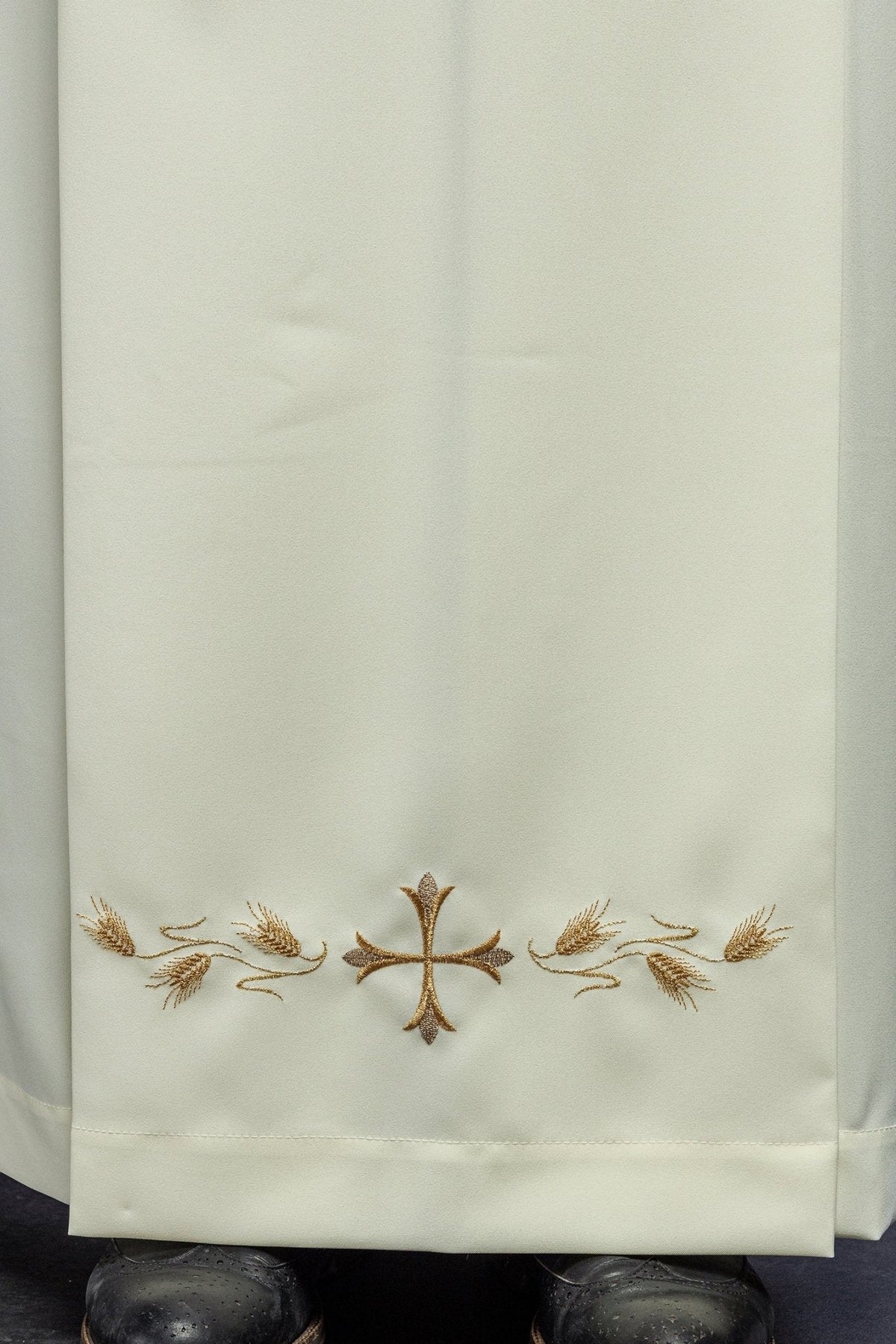 Alva sacerdotal creme em close-up da barra com cruz central e ramos de trigo bordados