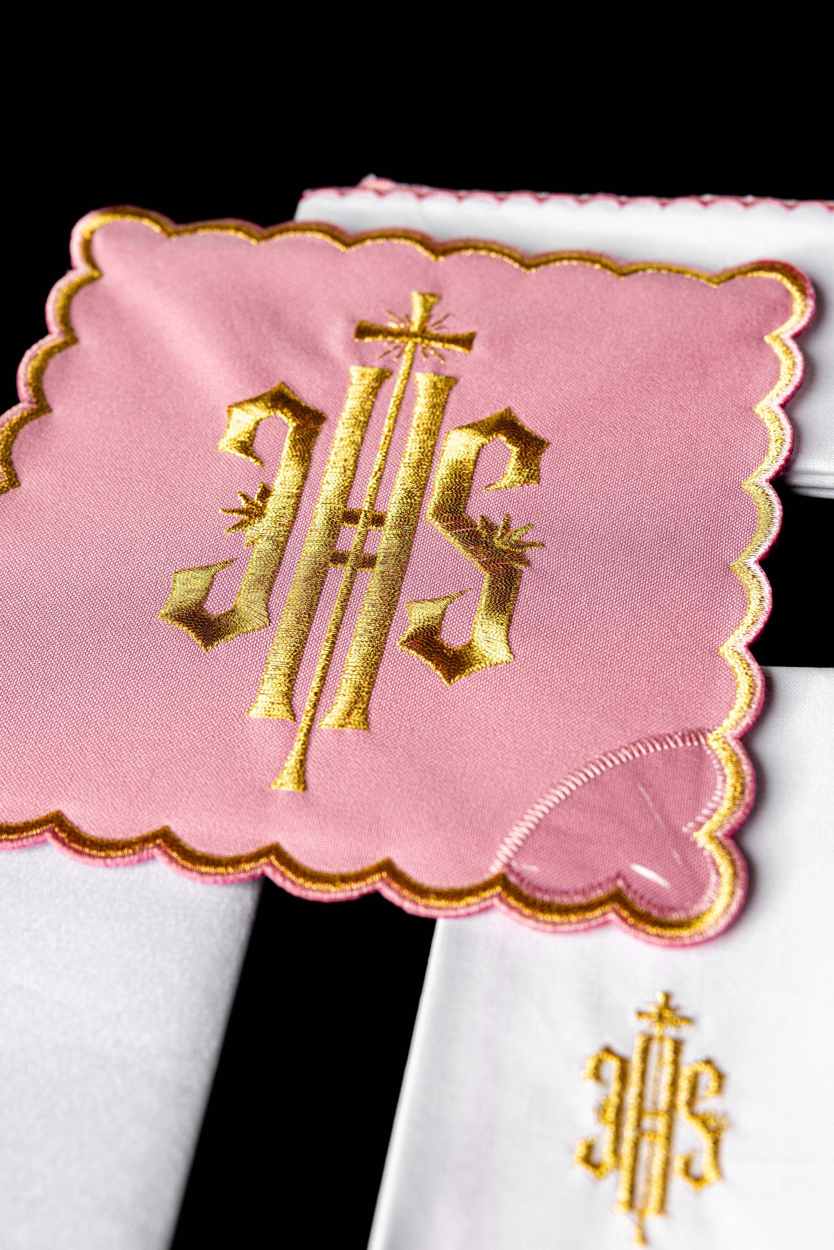 Alfaias litúrgicas rosa em close-up, com monograma IHS bordado em dourado