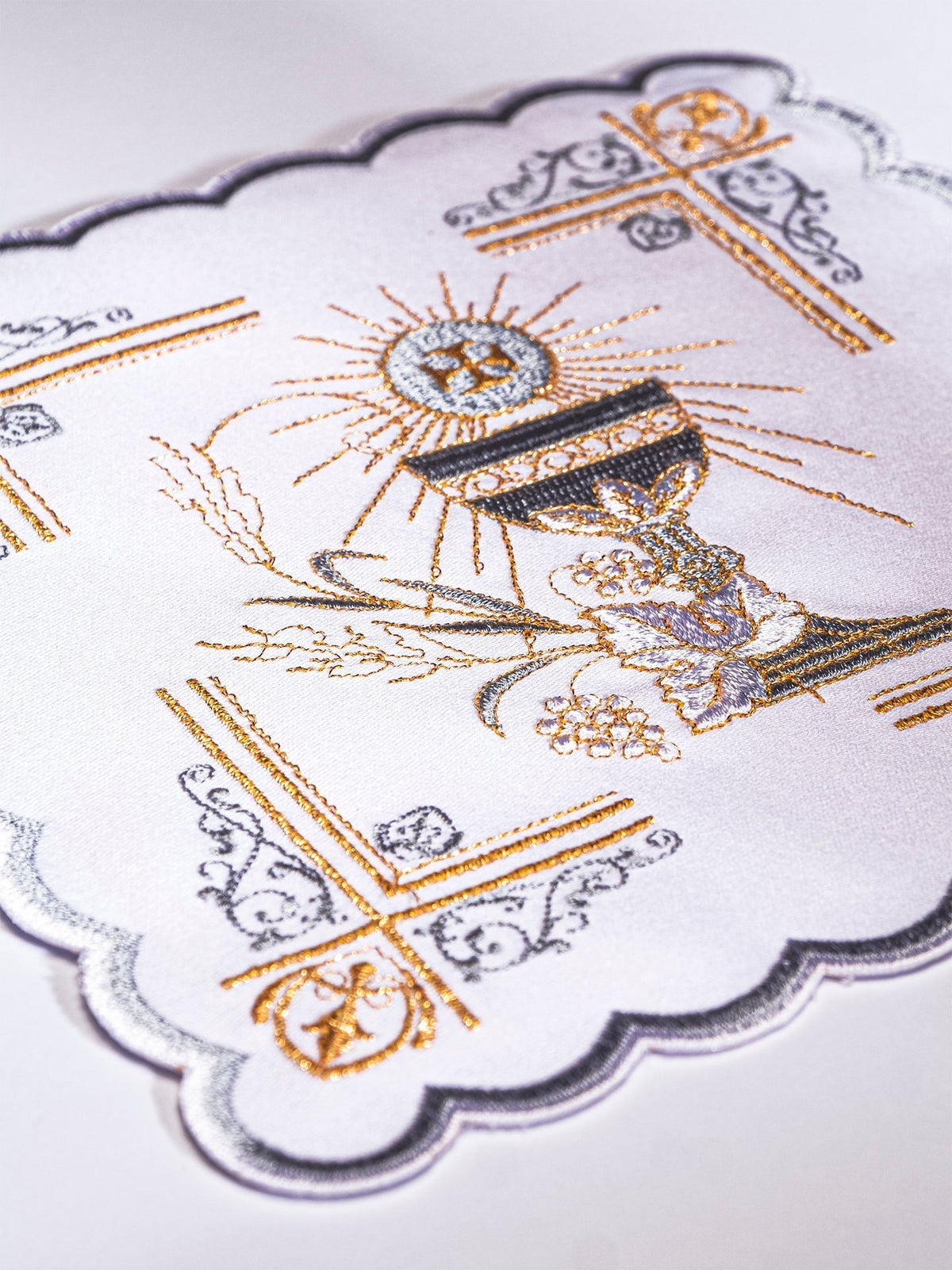 Alfaia litúrgica em close-up, com cálice, hóstia e bordado dourado e prateado