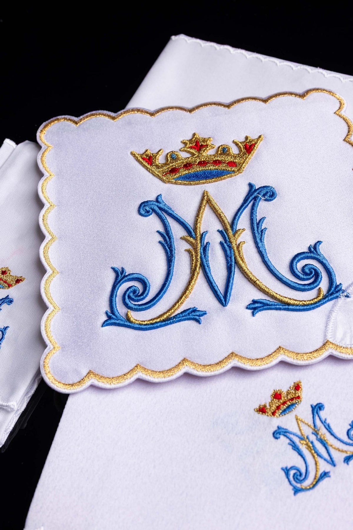 Alfaia litúrgica branca com pequeno monograma mariano azul e dourado e coroa bordada