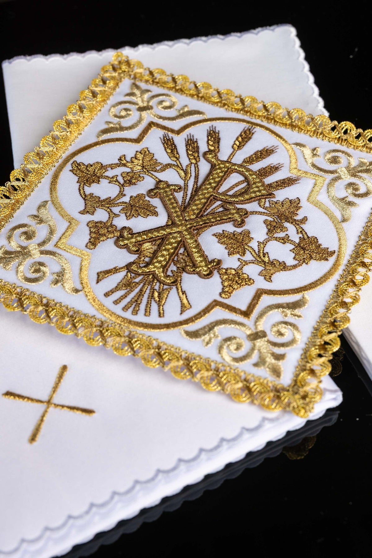 Conjunto de alfaias com detalhe aproximado do símbolo PAX bordado em dourado
