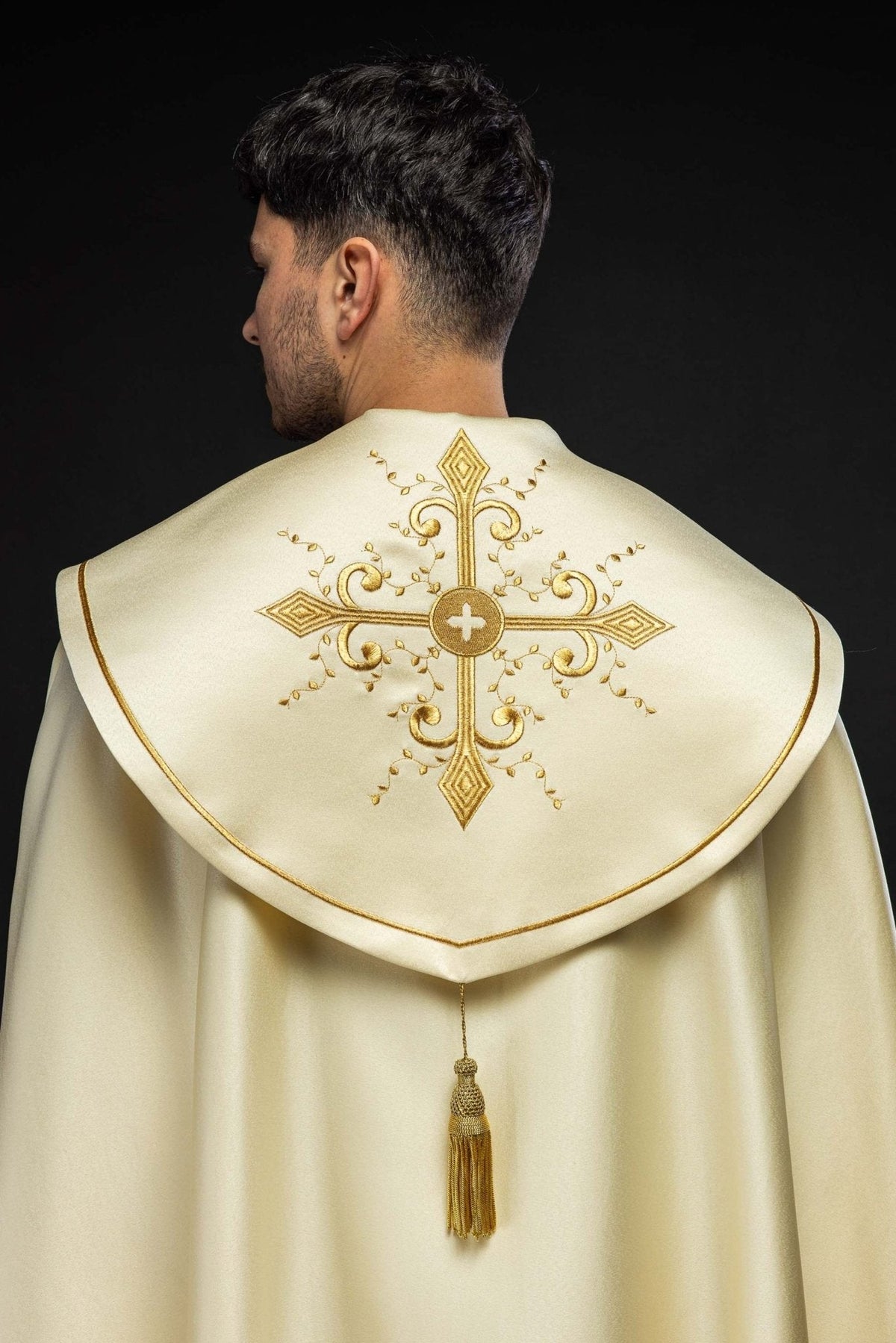 Capa de asperges litúrgica bordada creme vista de costas, com cruz dourada, acabamento dourado e borla