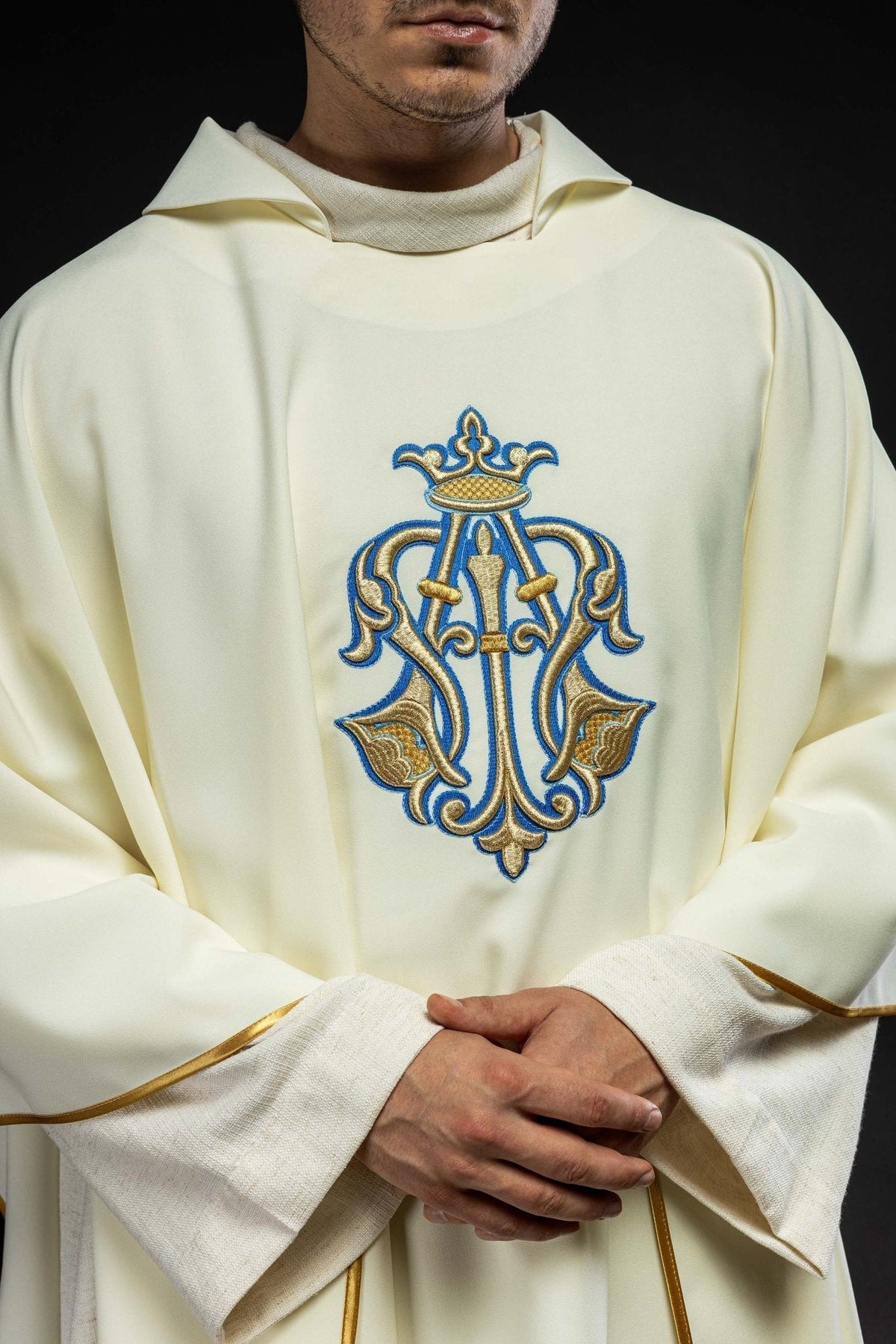 Casula creme em close, destacando o símbolo mariano bordado em azul e dourado