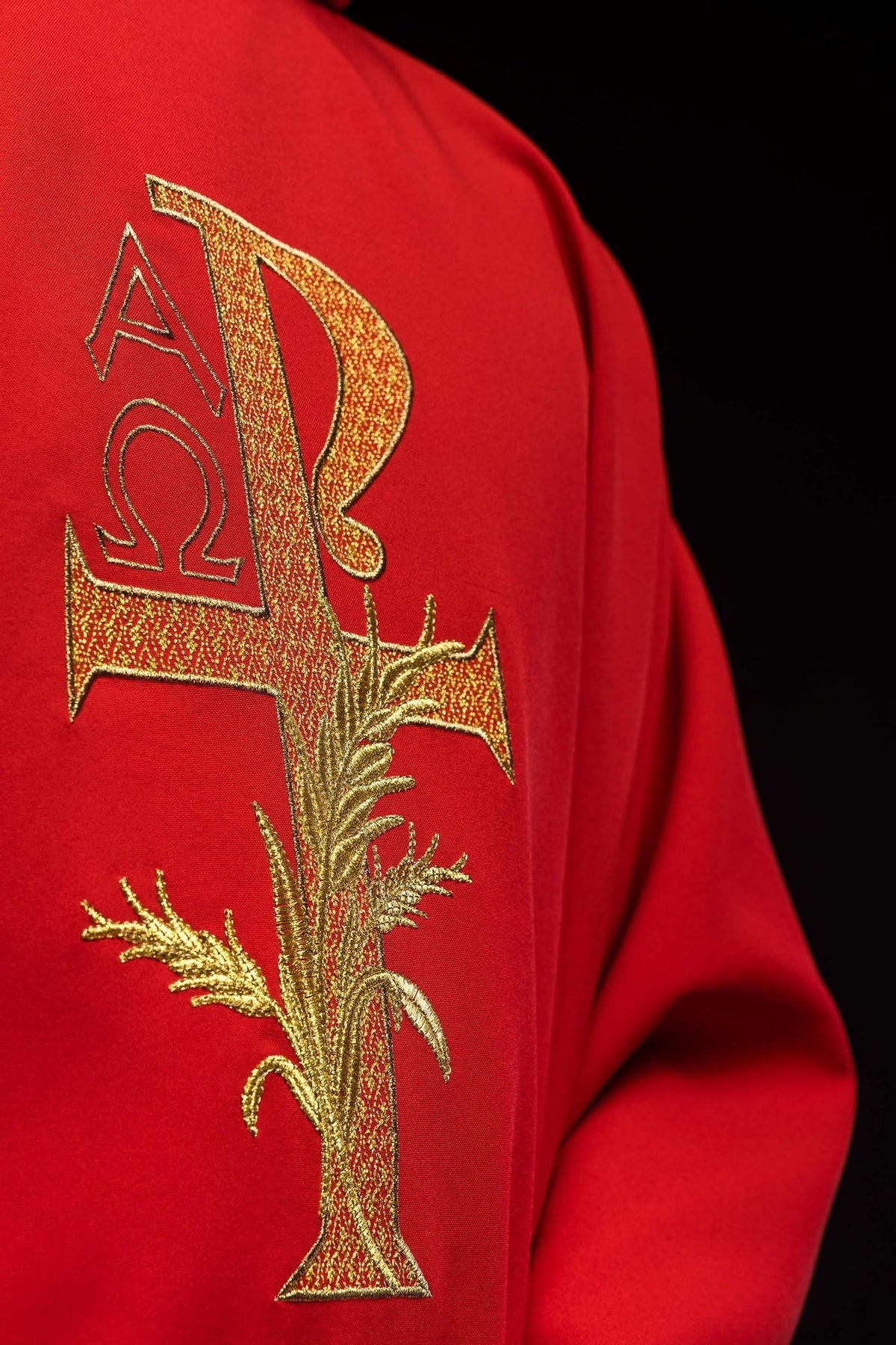 Casula vermelha, close-up do bordado dourado Alfa e Ômega com cruz e ramos