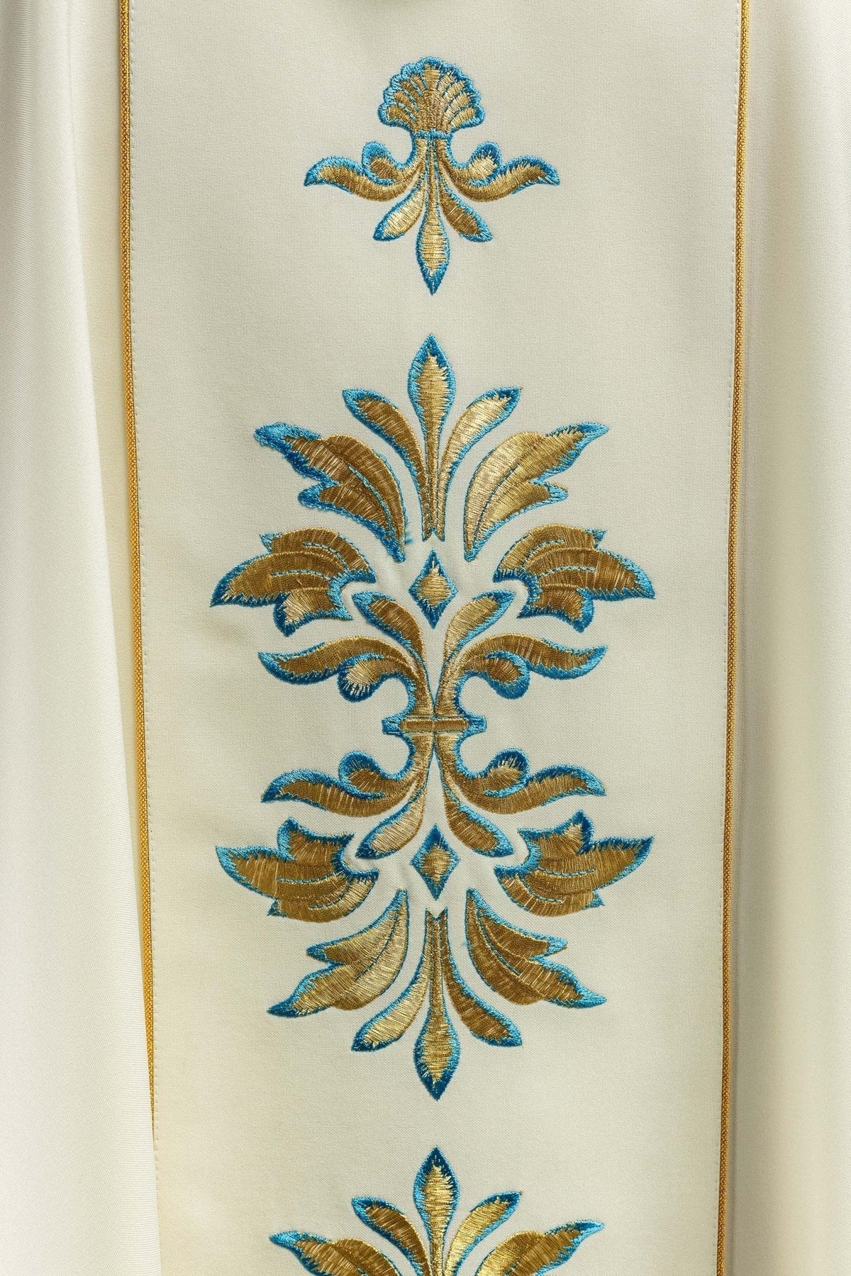 Casula creme com motivo mariano em close, destacando bordado floral azul e dourado na faixa central
