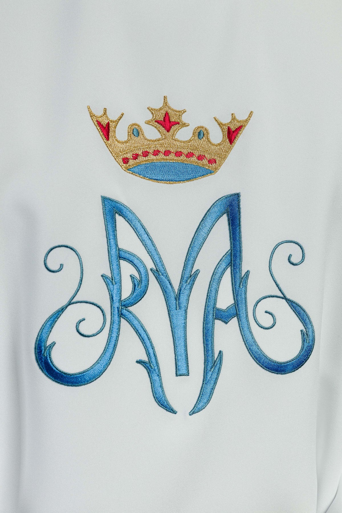 Casula branca mariana, close-up do bordado azul com coroa dourada e detalhes vermelhos