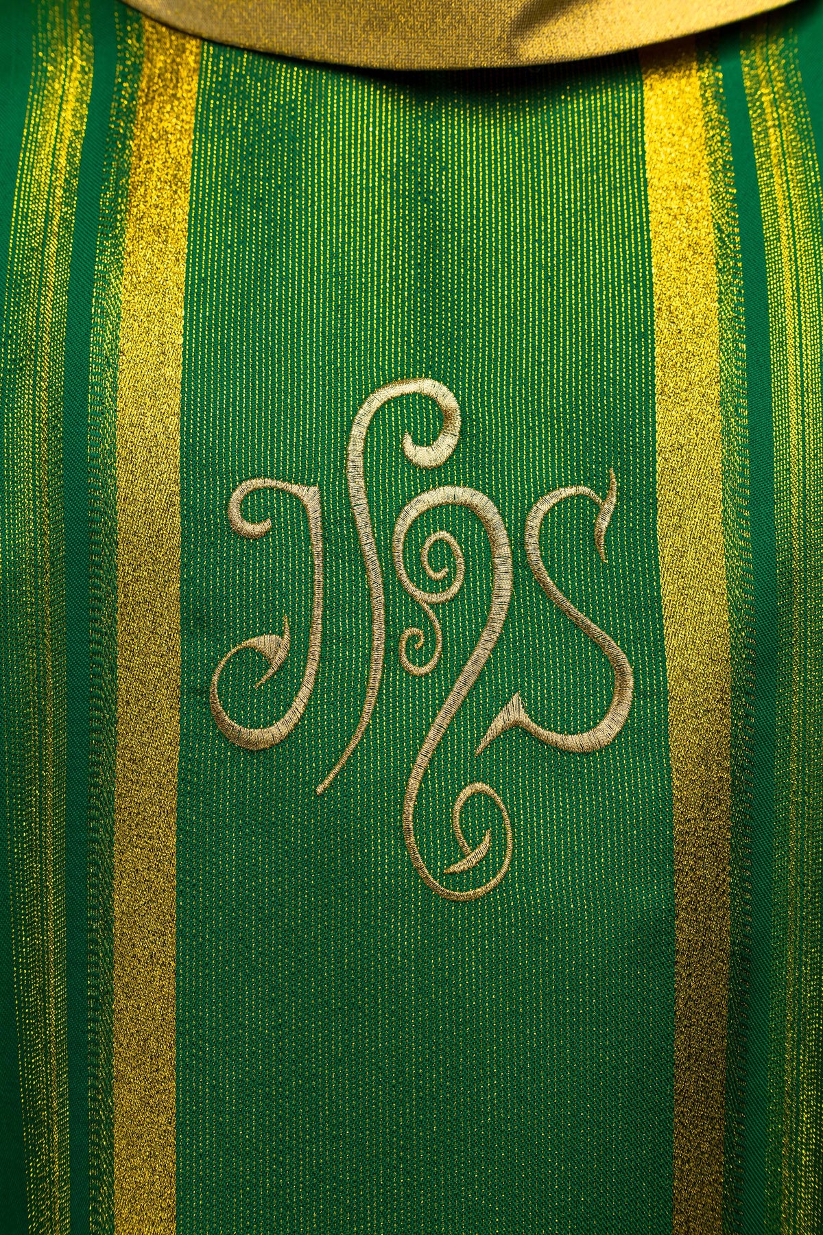 Casula verde IHS em close-up frontal, destacando o bordado dourado entre faixas douradas