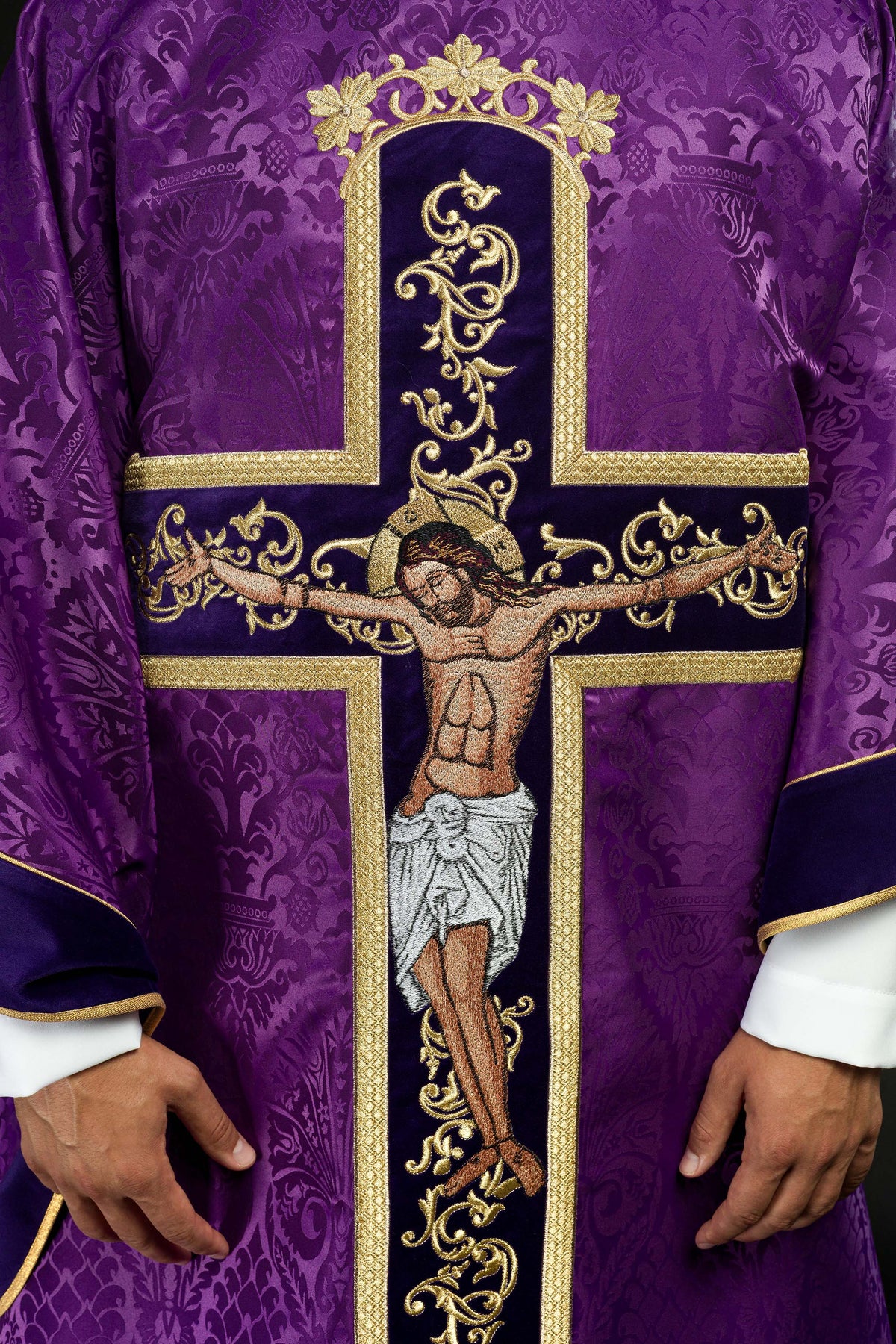 Casula roxa em close frontal, destacando Jesus Cristo crucificado e a cruz bordada