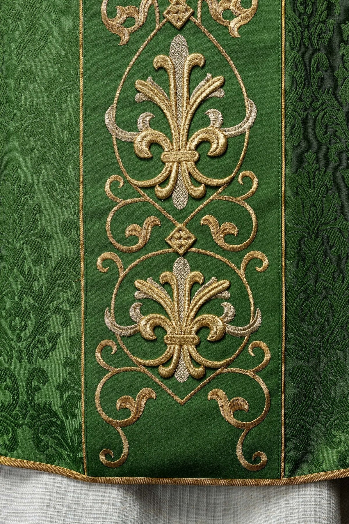 Casula verde com IHS bordado em detalhe, com flores-de-lis douradas na faixa central