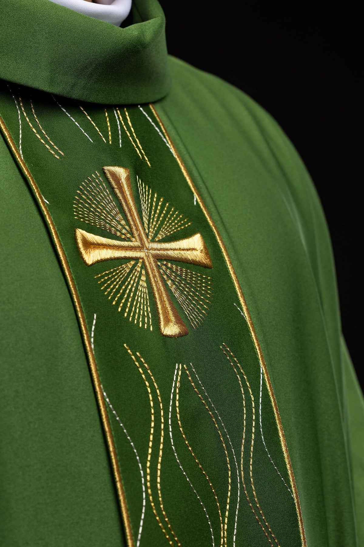 Casula verde com cruz bordada em close-up, destacando a cruz dourada e os fios decorativos