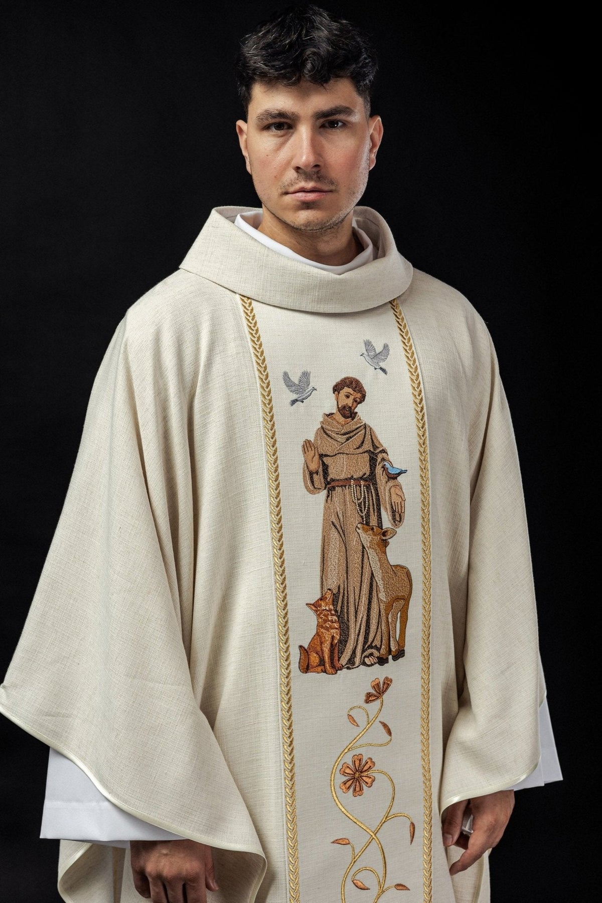 Casula bordada com imagem de São Francisco, em tom ecru, vista frontal com bordas douradas e flores
