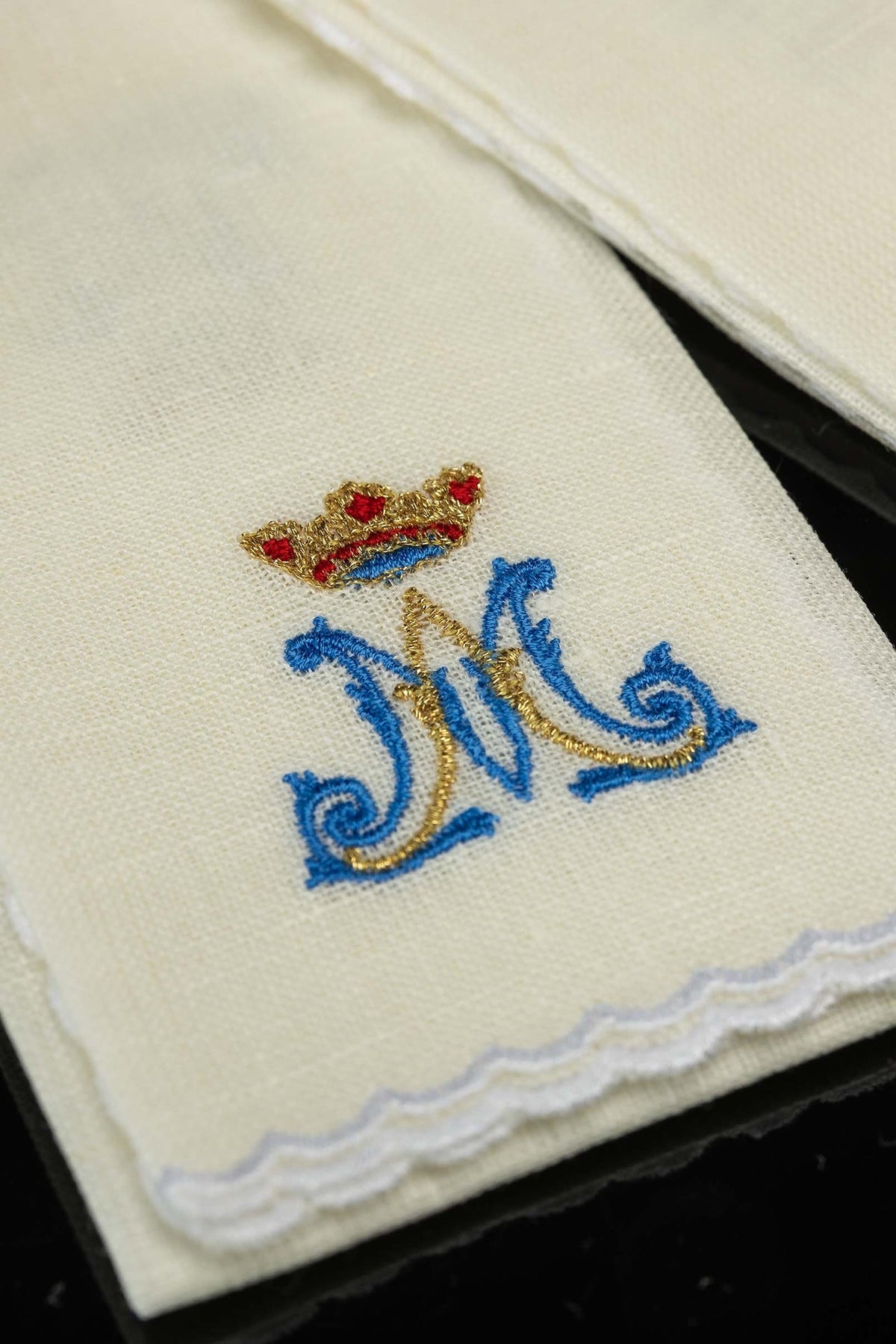 Sanguíneo de linho em close-up, com monograma azul e dourado, coroa bordada e acabamento branco