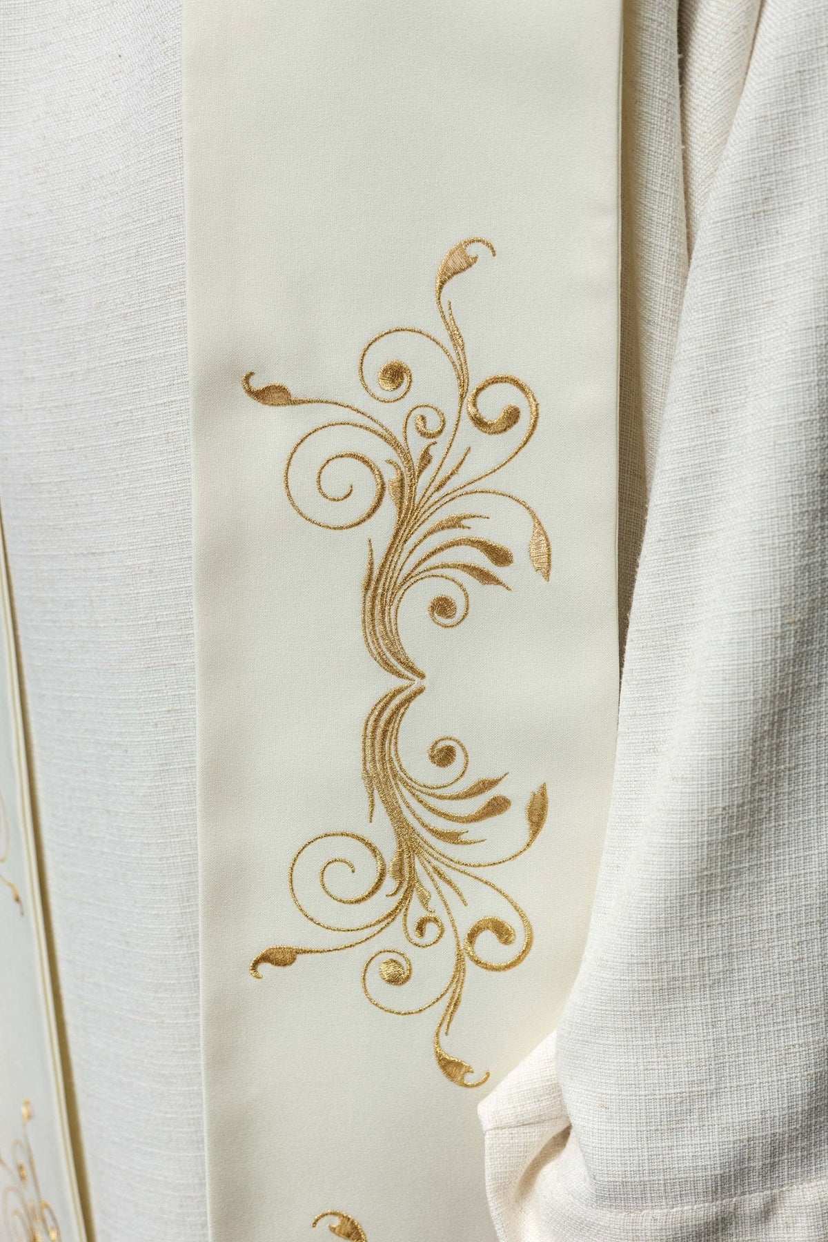 Estola creme com IHS, close do arabesco floral dourado na faixa