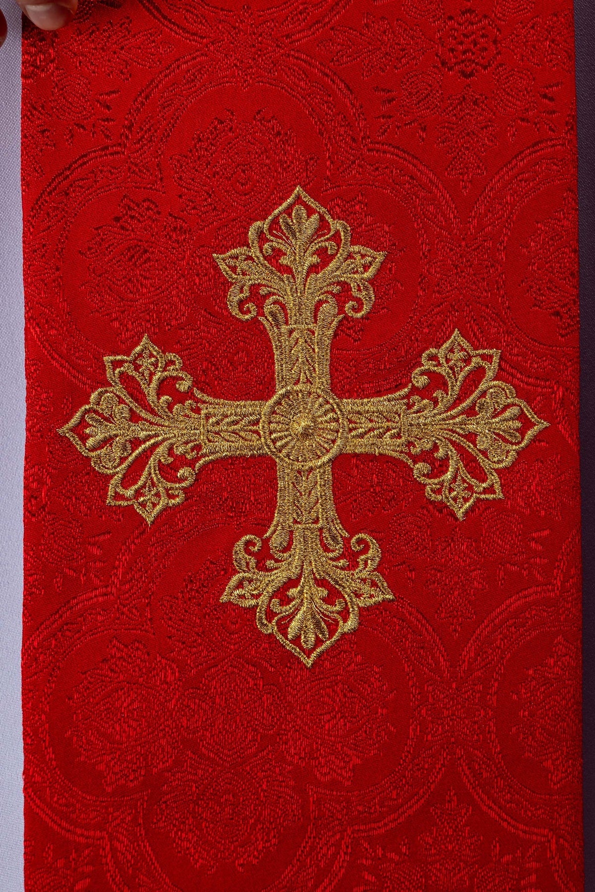 Estola vermelha em close-up, com detalhes do bordado dourado da cruz