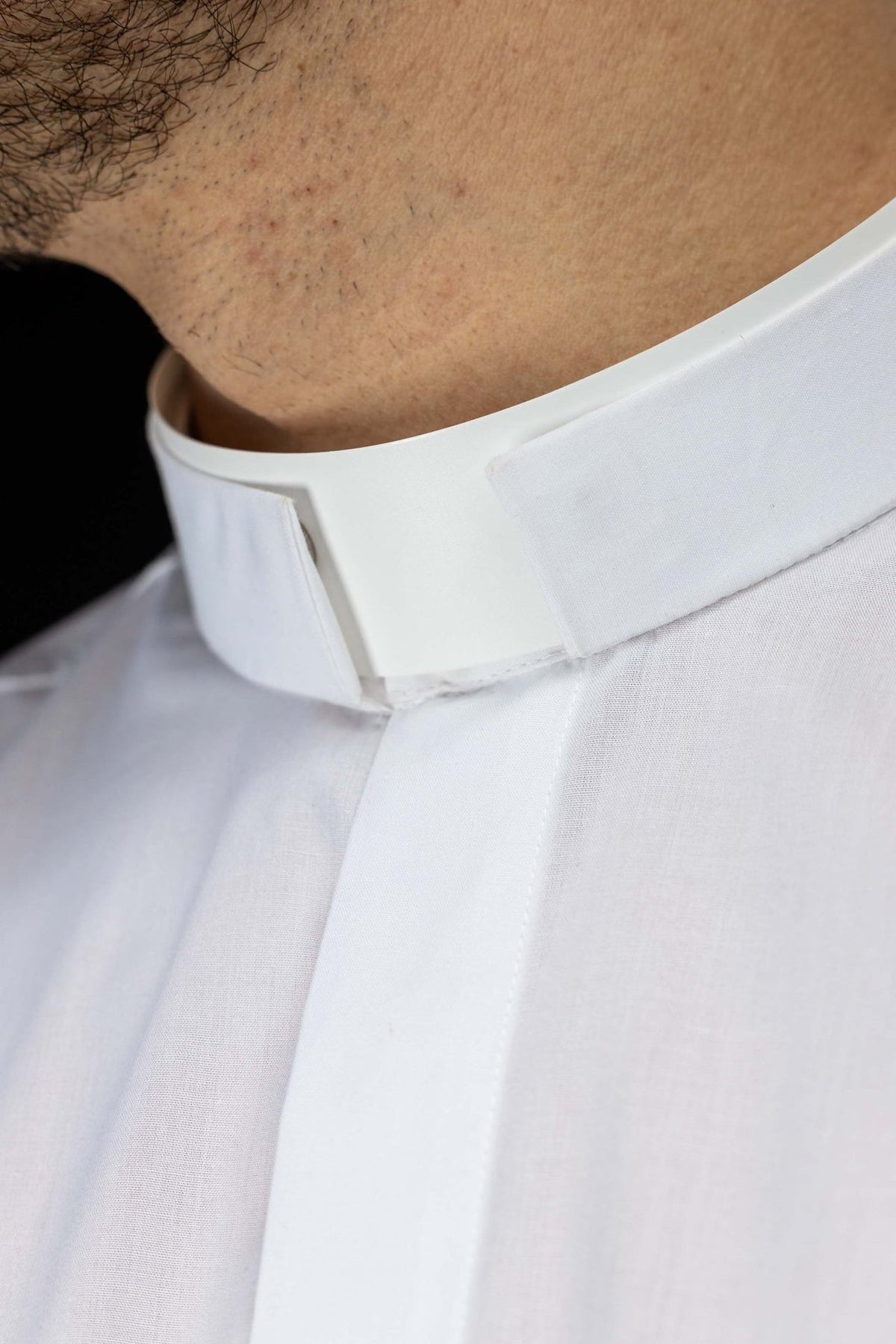 Camisa clerical branca em close-up, com colarinho romano e vista da abertura frontal