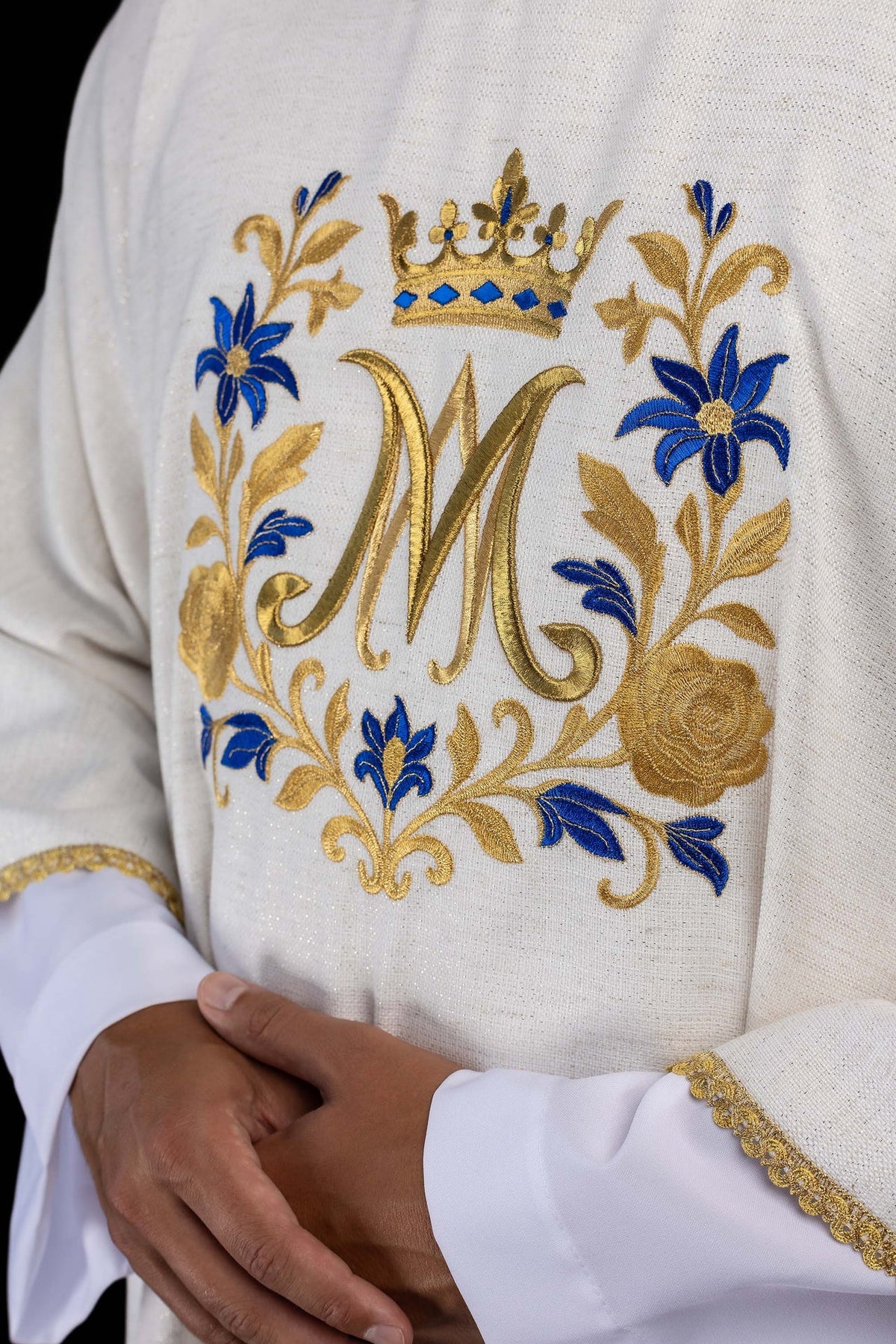 Dalmática marfim ecru em close-up lateral do bordado mariano dourado e azul