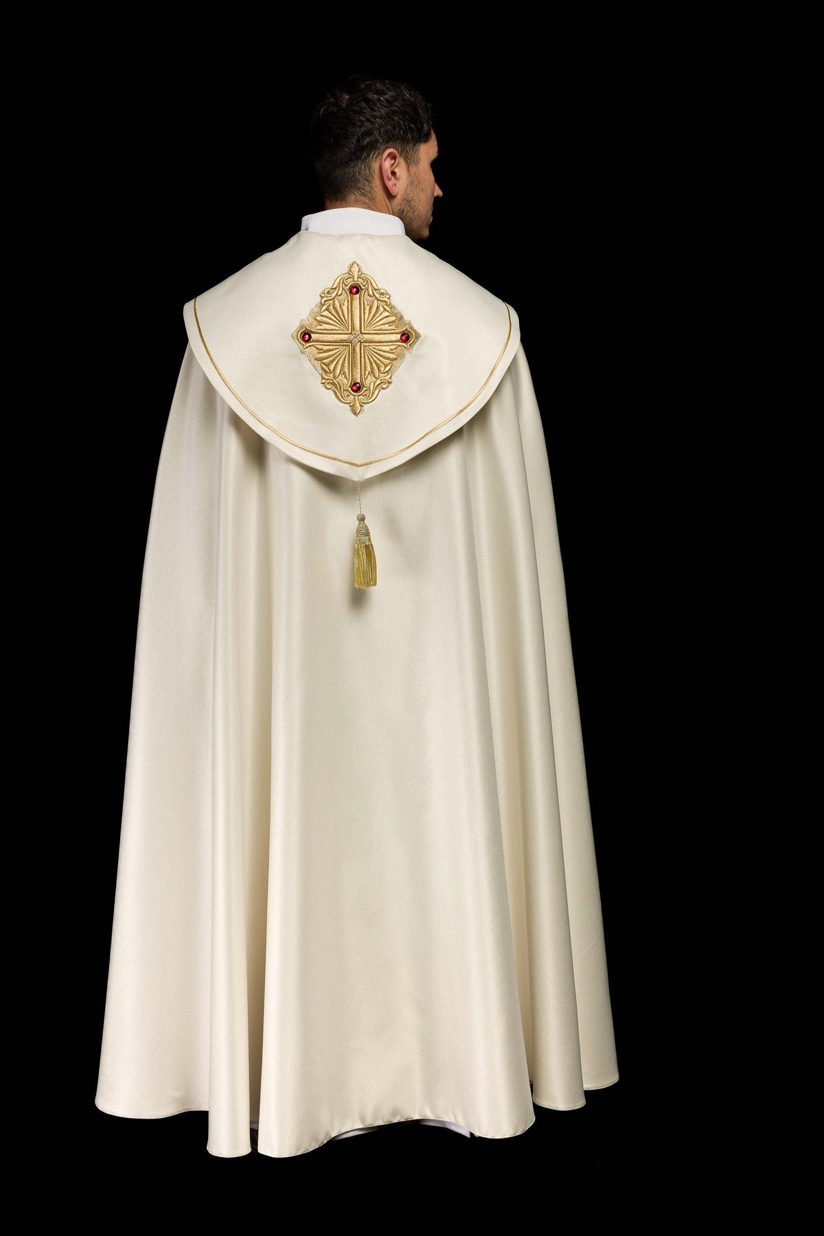 Close da cruz dourada bordada com pedras vermelhas na capa de asperges