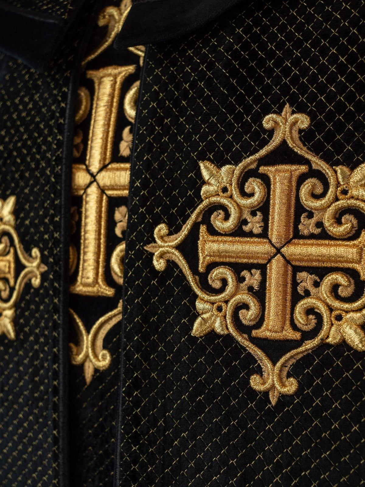 Capa litúrgica preta, close do bordado dourado de cruz na faixa