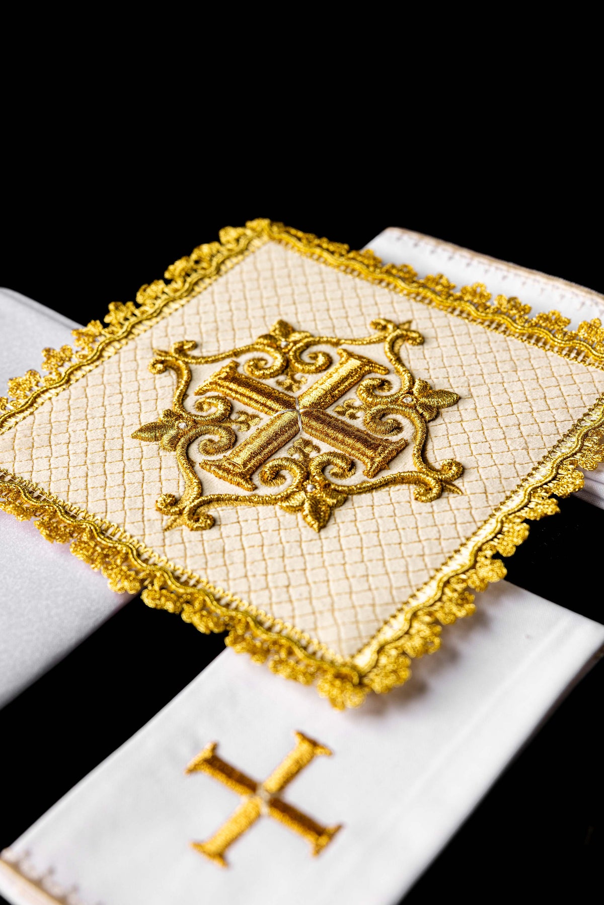Conjunto de alfaias com cruz central bordada e acabamento dourado, vista inclinada
