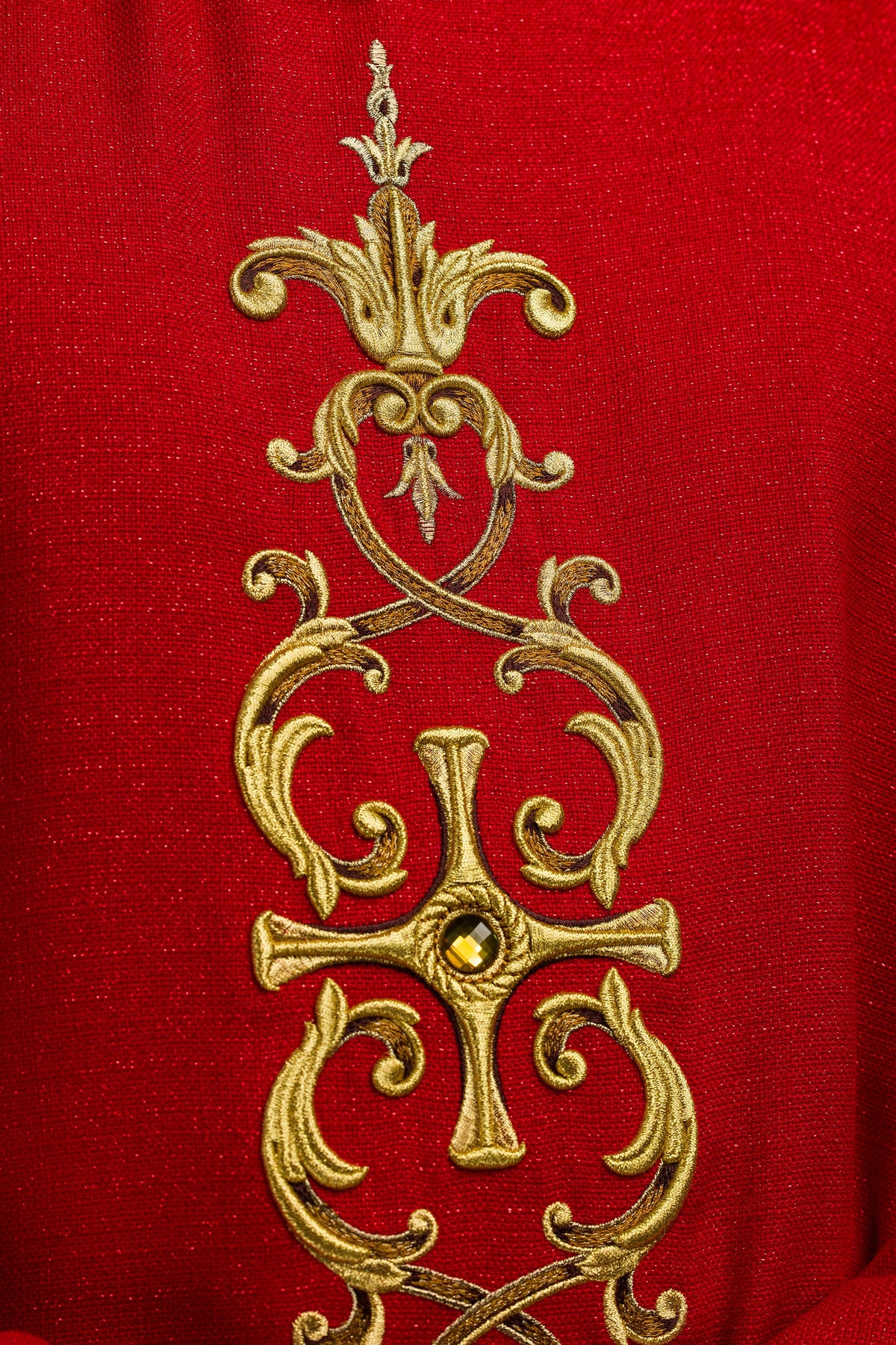 Casula vermelha em close-up, destacando bordado dourado e pedra central