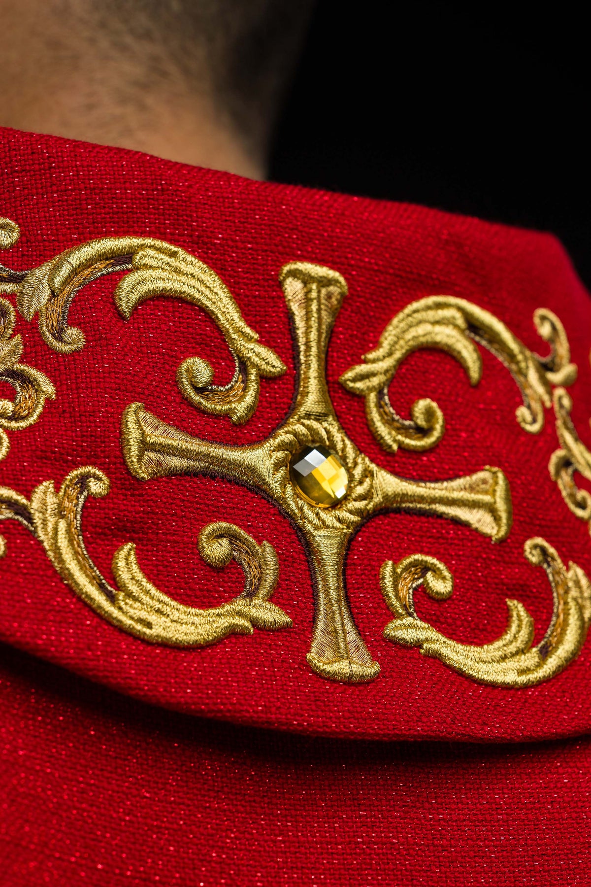 Casula vermelha em close-up da cruz dourada com pedra central