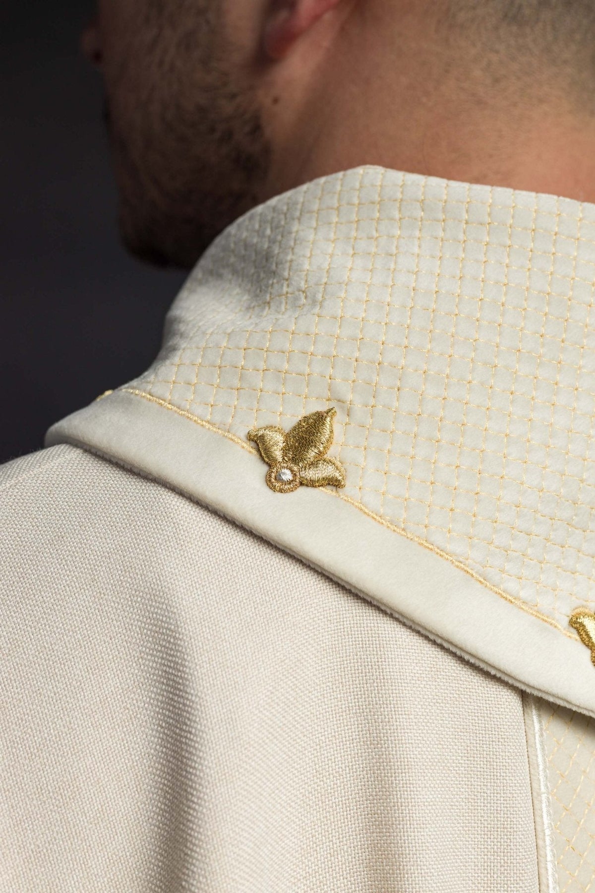 Casula creme, detalhe lateral da gola com padrão em losangos e bordado dourado