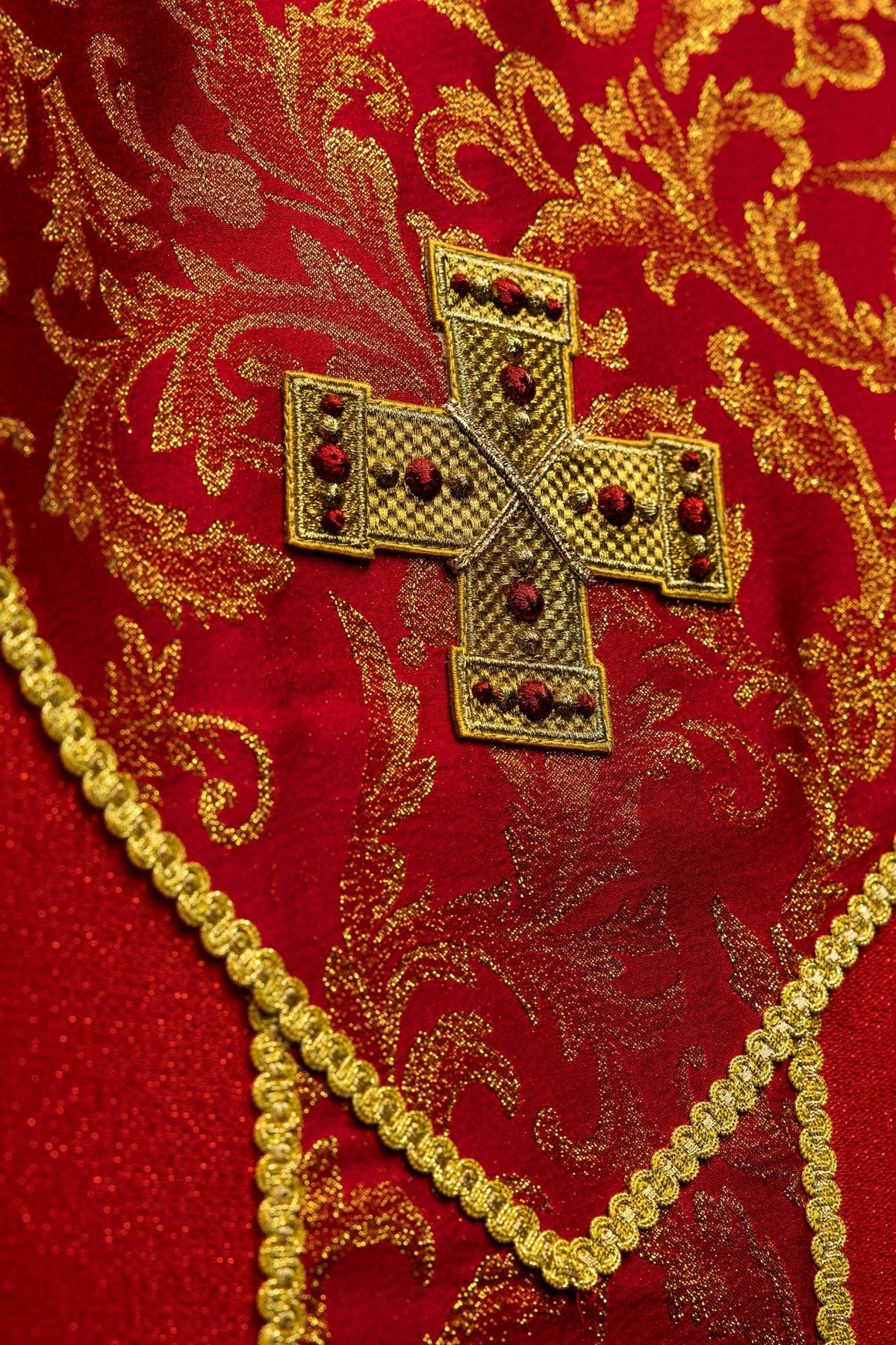 Casula vermelha em detalhe lateral, mostrando galão dourado na manga e tecido vermelho