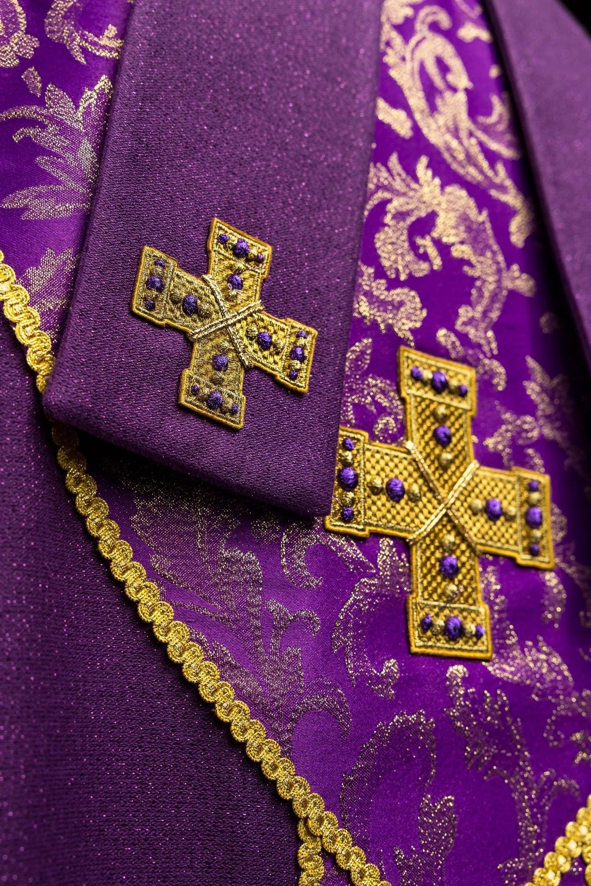 Mitra roxa em detalhe, com cruz bordada sobre tecido liso e jacquard
