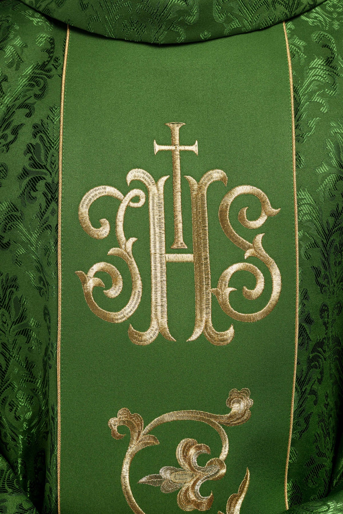 Casula verde com bordado IHS em close-up, destacando o monograma IHS dourado