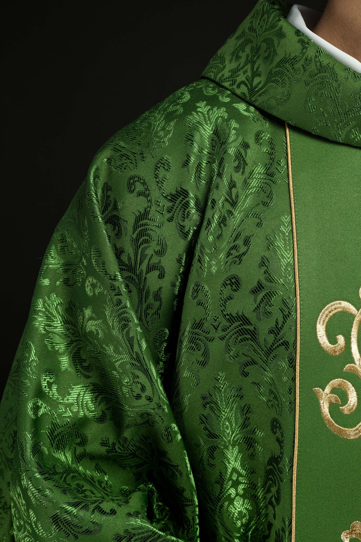 Casula verde com bordado IHS em close-up lateral, com tecido verde adamascado e faixa dourada